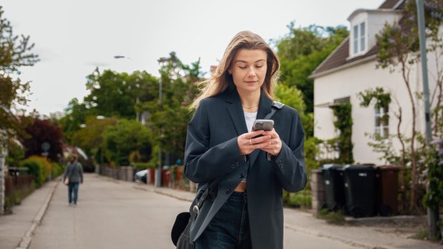 Bilde av en jente som går nedover en gate med mobil i hånden