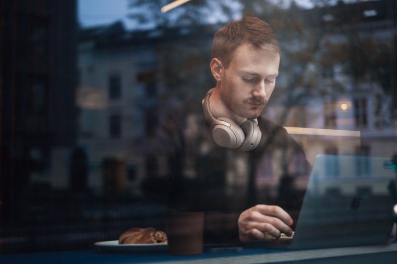 A student sitting at a computer, visible through a window, focused on their screen.
