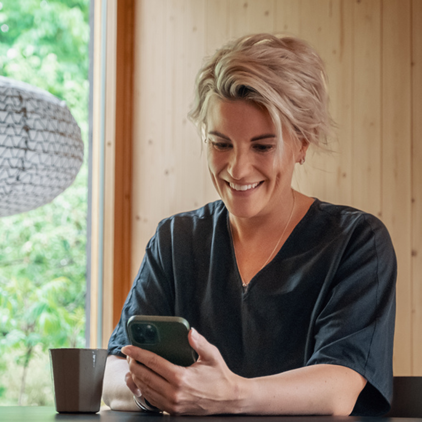 Foto av smilende kvinne som ser på mobilen.