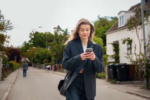 Bilde av en jente som går nedover en gate med mobil i hånden